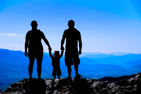 Family with toddler on mountain top silhouette holding hands looking at mountains