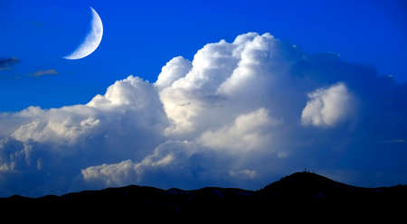 Mountains sky billowy white thunder clouds and crescent moon in the wildernessの写真素材