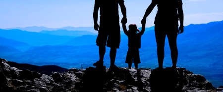 Family with toddler on mountain top silhouette holding hands looking at mountains