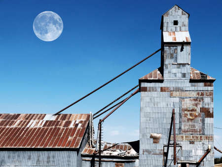 Old abandoned granary with painted signs and blue sky with full moonの写真素材