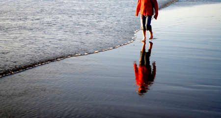Young child wearing a red jacket playing on the beach of the ocean with waves rolling inの写真素材