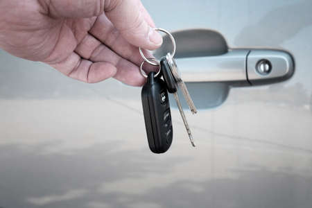 Hand holding car keys in front of grey car door