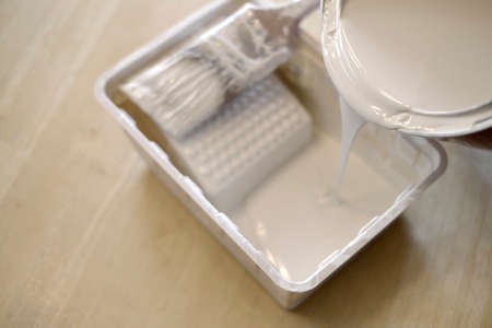 Pourint white paint into plastic paint bin with paintbrush for painting homeの写真素材