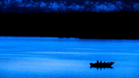 Fishermen in a boat on a lake in the evening or early morning lightの写真素材