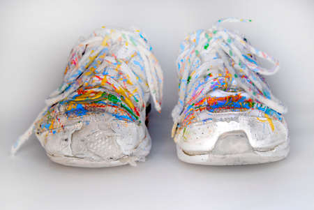 Old worn white shoes sneakers splattered in colorful paintの写真素材