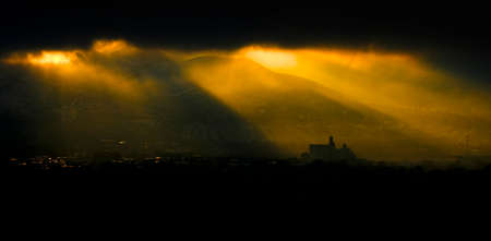 Sunbeams from sunlight streaming down brightly on a town with mountains cityscape lightの写真素材