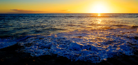 Ocean Water Wave Washing Up on Beach Rocks with Sunset Sunshine splashの写真素材