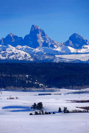 Teton Mountains Grand Tetons in winter with old cabin homestead building in fieldの写真素材