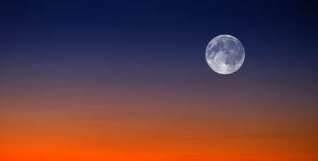 Sunset and Full Moon in sky in landscape on horizon with orange and blue lightの写真素材