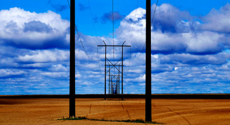 Powerlines in field with blue sky and clouds representing utilityの写真素材