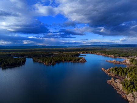 Aerial view from a drone flying above a lake with forest sky and cloudsの写真素材