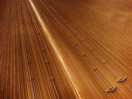 Furrowed farm field plowed with sprinklers spraying water irrigation for farmingの写真素材