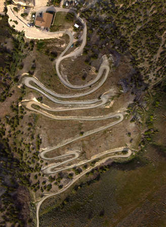 Aerial view from a drone flying above a winding curved dirt road on mountainsideの写真素材