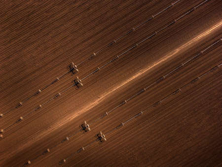 Furrowed farm field plowed with sprinklers spraying water irrigation for farmingの写真素材