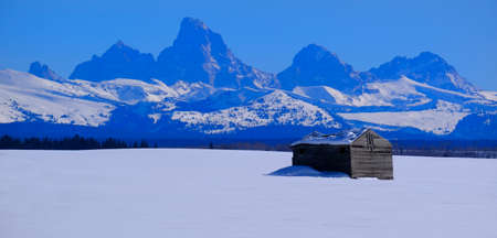Teton Mountains Grand Tetons in winter with old cabin homestead building in fieldの写真素材