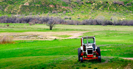 Old tractor for working on farm fields green with hills and mountainsの写真素材