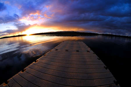 Lake at sunset or sunrise with clouds and sky reflection reflecting in water colorsの写真素材