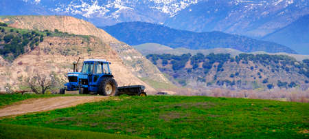 Old tractor for working on farm fields green with hills and mountainsの写真素材