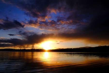 Sunset and storm clouds over lake with pine trees wilderness reflectionの写真素材