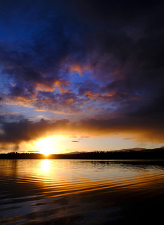 Sunset and storm clouds over lake with pine trees wilderness reflectionの写真素材