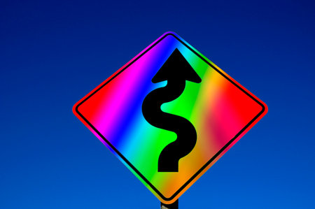 Gay Pride LGBTQ Rainbow colored street sign with curves against blue sky