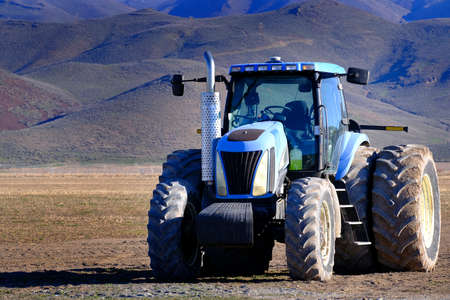 Blue tractor in dirt field on farm for spring planting farming business