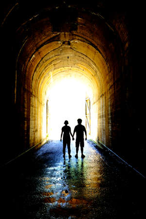 Two people in love holding hands silhouetted silhouette at tunnel exit togetherの写真素材