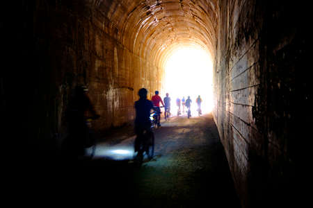 Group of people bikers biking through dark tunnel with headlights on Hiawatha Trailの写真素材