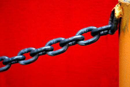 Chain for security hanging from yellow metal pole with red wall in backgroundの写真素材