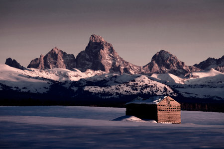 Teton Mountains Sunset Light Grand Tetons in winter with old cabin homestead building in fieldの写真素材