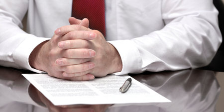 Businessman at desk with pen and contract making hand gesturesの写真素材