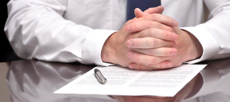 Businessman at desk with pen and contract making hand gesturesの写真素材