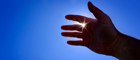 Hand reaching up towards heaven seeking help with sunstar sunshine inspiration guidanceの写真素材