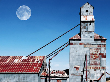 Old abandoned granary with painted signs and blue sky with full moonの写真素材