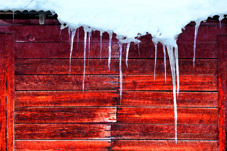 Icicles hanging off roof of all weathered red barn snall fallingの写真素材