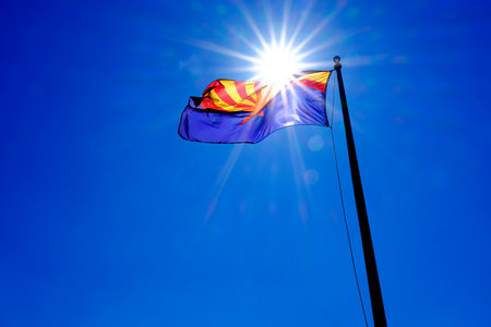 Arizona state flag flying in breeze on flagpole with sunshine sunstar in blue skyの写真素材