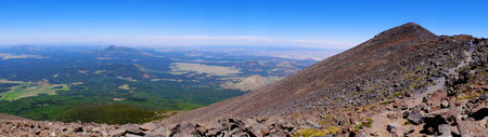 Panoramic image of a person hiking to the top of a mountain summit in wilderness with green valley belowの写真素材