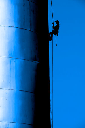 Silhouette of professional person on ropes dangling in air painting sign on side of building siloの写真素材