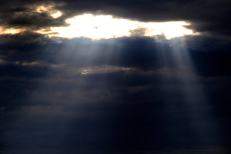 Long sunrays shining above mountains in storm clouds sun rays