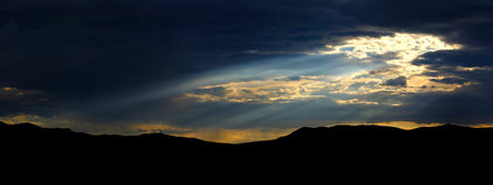 Long sunrays shining above mountains in storm clouds sun rays