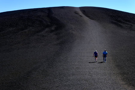 People tourists hiking on black lava cinder Inferno Cone at Craters of the Moon National Monumentの写真素材