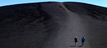 People tourists hiking on black lava cinder Inferno Cone at Craters of the Moon National Monumentの写真素材