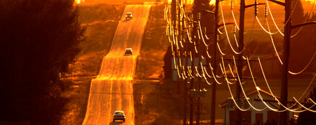 Cars driving on old country road at sunset of sunrise power lines