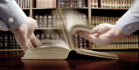 Hands turning pages in old  book with library in background flipping page looking for knowledgeの写真素材