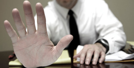 Business man sitting at desk holding up hand to stop communicationの写真素材