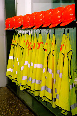 Detail of safety gear hard hats and vests hanging on wall of factory for health and emergency emergenciesの写真素材