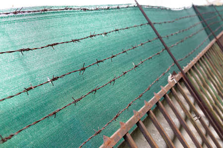 Green metal fence with barbed wire.の写真素材