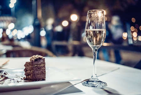 glass of white wine with chocolate cake on white table in a terrace restaurant evening with beautiful bokeh backgroundの写真素材