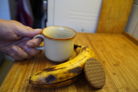 Hand holding a cup of coffee and two bananas on a wooden tableの写真素材