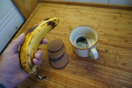 A man's hand holds a banana and a cup of coffee.の写真素材